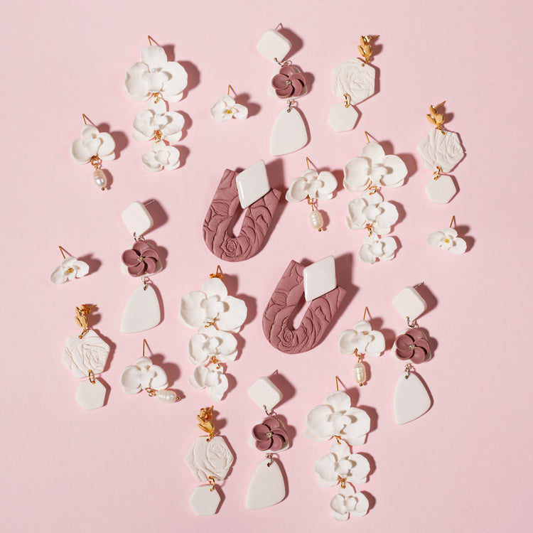 Pendientes colgantes con formas geométricas y textura floral en blanco y dorado.