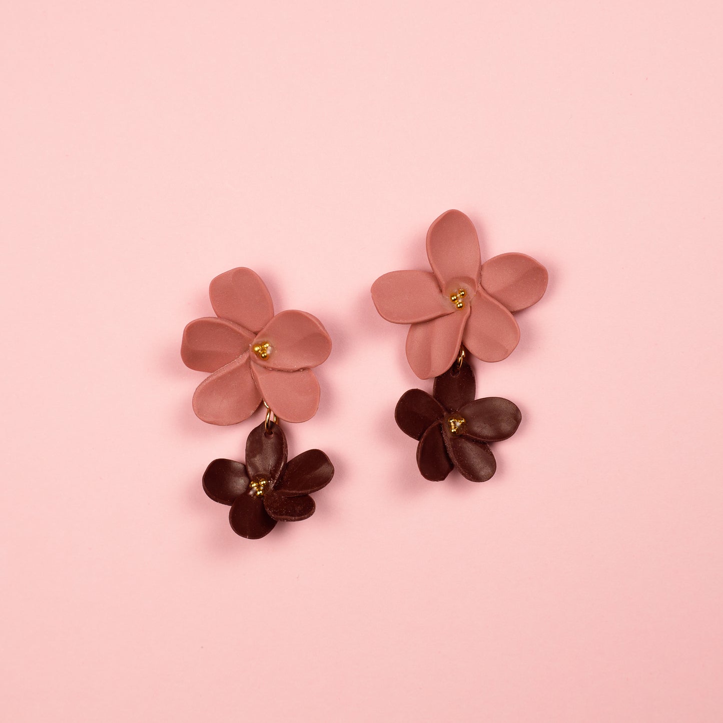 Pendientes colgantes hechos a mano en arcilla polimérica y acero inoxidable. Dos flores rosa y burdeos de distintos tamaos dispuestas en cascada y con detalles en dorado.