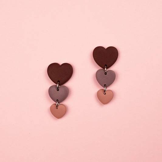 Pendientes hechos a mano en arcilla polimérica con diseño en cascada de tres corazones en distintos tamaños en burdeos, rosa y lila.