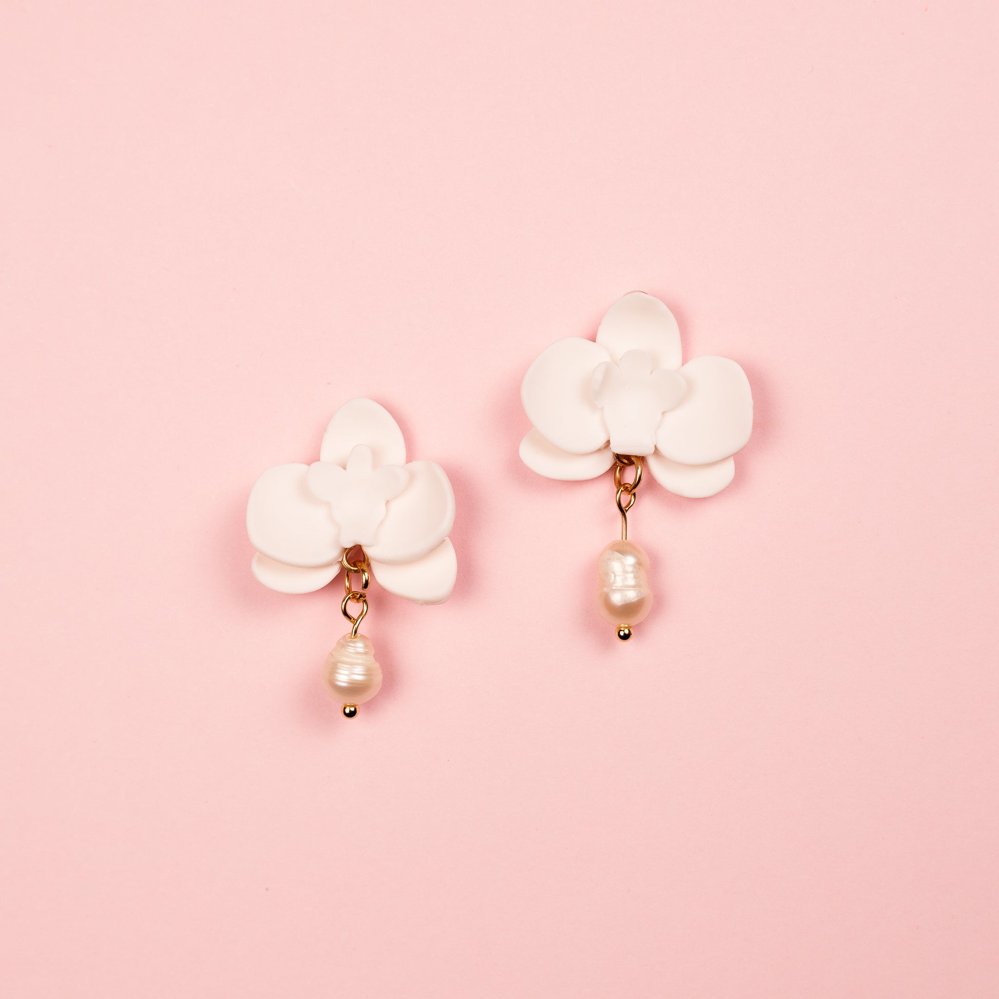 PEndientes hechos a mano con arcilla polimérica y acero inoxidable en forma de orquídea adornados con una perla.