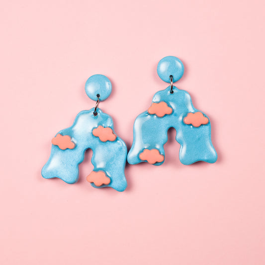 Pendientes de arcilla polimérica y acero inoxidable hechos a mano con forma de arco decorado con nubes en color azul y coral pastel.