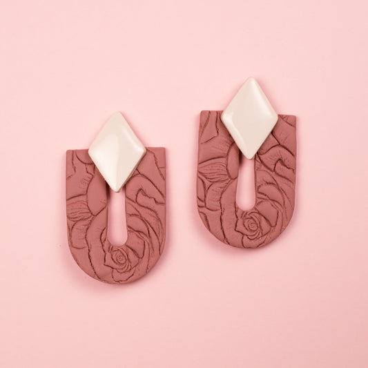 Pendientes hechos a mano de arcilla polimérica y acero inoxidable con forma de arco y rombo y textura floral en tonos rosas y blancos.
