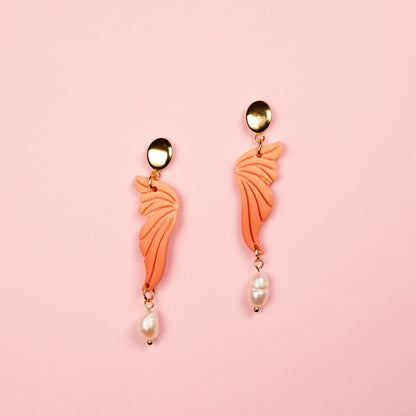 Pendientes colgantes de arcilla polimérica con forma de alas hechas a mano. Tienen detalles dorados y perlas de río blancas.